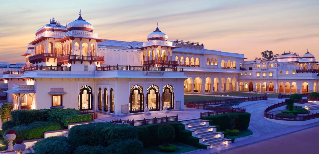 Rambagh Palace Jaipur glowing beautifully in soft lights, showcasing its royal architecture, lush gardens, and timeless grandeur during a peaceful evening view